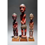 Three Baule colon standing figures Ivory Coast painted red, including a female and two males,