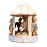 A Yoruba model house Nigeria with a lift off roof supported by five posts, revealing a seated figure