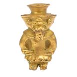 A Tairona style figure amulet Colombia gilt copper, wearing a rimmed hat and with a coca leaf