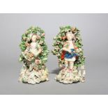 A pair of Derby figures of children, c.1770, each standing before tall flowering bocage with further