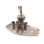 A Persian metalware ewer, six tot cups and a tray, the ewer of baluster form, chased foliate