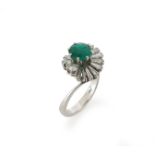 An emerald and diamond cluster ring, the circular-cut emerald is set within a surround of circular