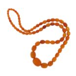 A single-row amber bead necklace, the oval beads graduate from 8 - 30mm long, 95cm long, 82.4g