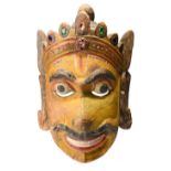 An Indian mask a crowned deity with inset paste and painted decoration, 43cm high.