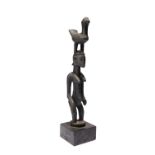 A Senufo standing female figure Ivory Coast with a bird crest and having a black oily patina,
