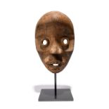 A Dan mask Ivory Coast with an encrusted patina, 25.7cm high, on a stand. (2) Provenance Roger