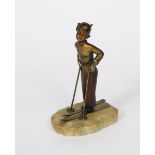 A patinated bronze model of a young boy skier, modelled standing resting, on a textured,