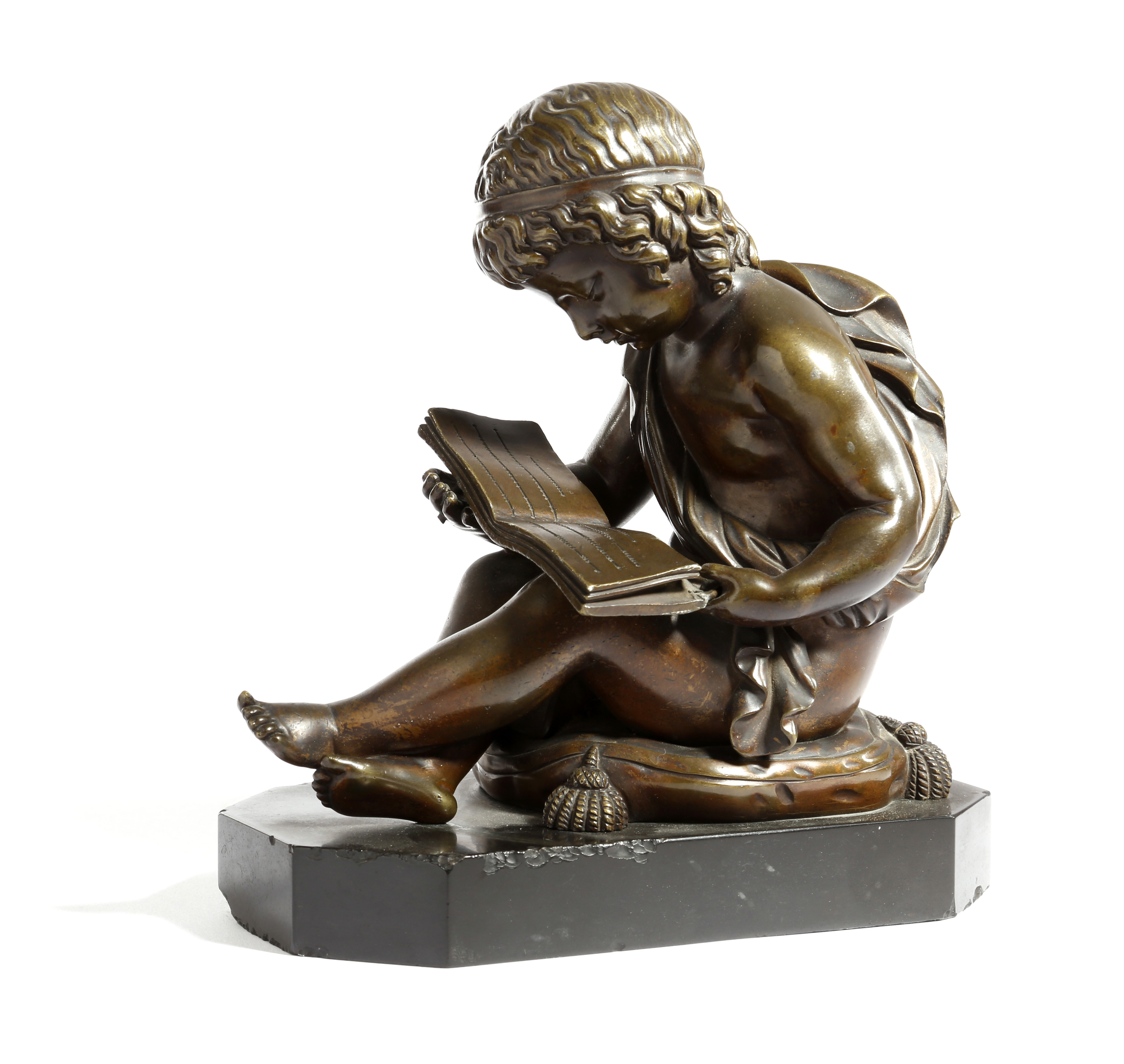 A FRENCH BRONZE OF A CHERUB READING C.1860-70 the young boy seated on a tasselled cushion holding