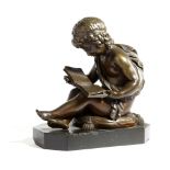 A FRENCH BRONZE OF A CHERUB READING C.1860-70 the young boy seated on a tasselled cushion holding
