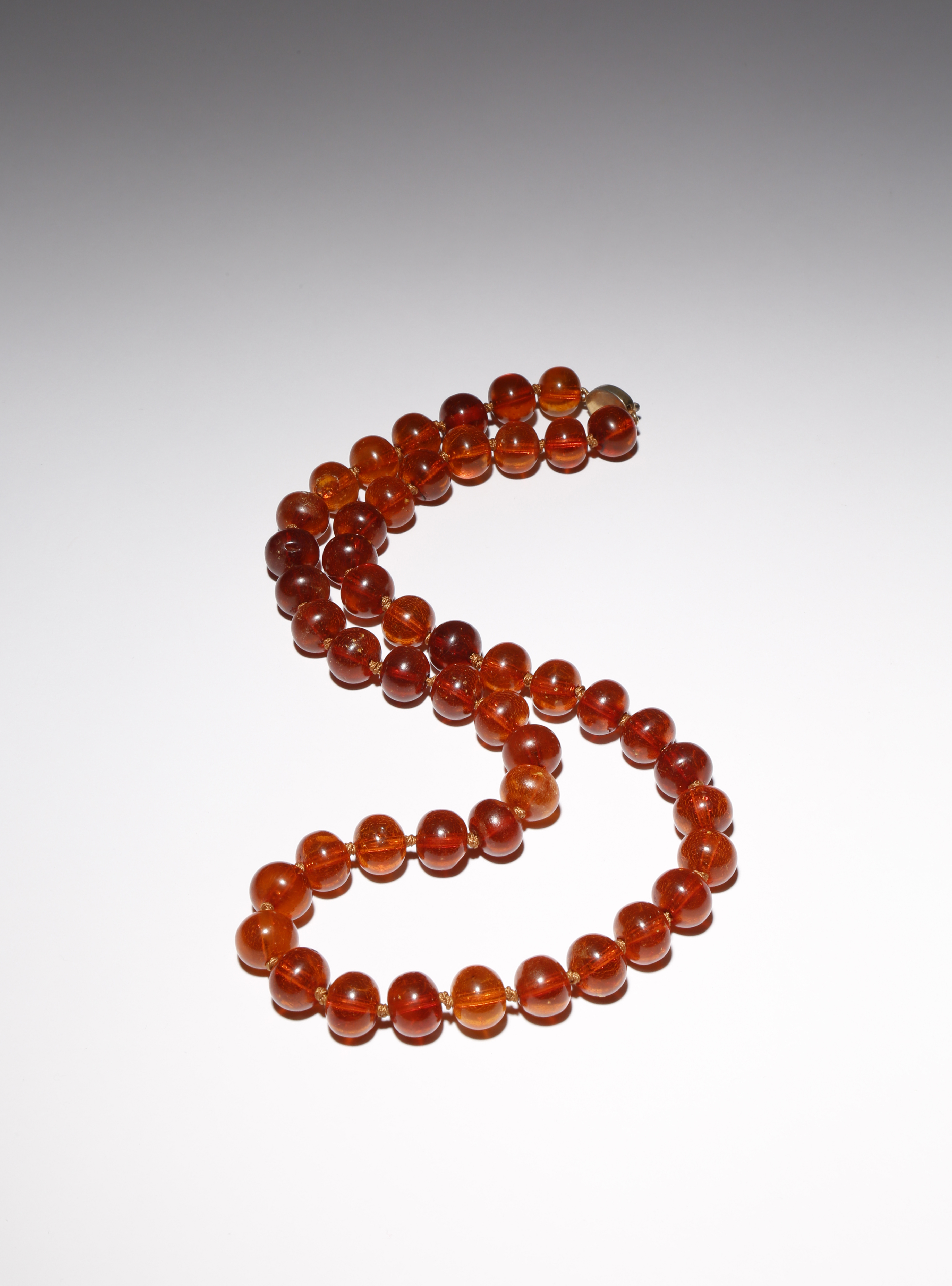 AN AMBER BEAD NECKLACE 20TH CENTURY With compressed circular beads, the gilt-metal clasp set with