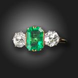 An emerald and diamond three-stone ring, the emerald-cut emerald is claw set with an old circular-