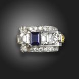 An Odeonesque sapphire and diamond ring, set with an emerald-cut sapphire within scrolling border of