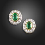 A pair of emerald and diamond cluster earrings, the oval-shaped emeralds are set within a surround