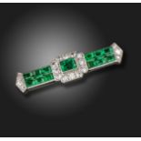 An Art Deco emerald and diamond brooch by Cartier, set with a rectangular emerald within tapered