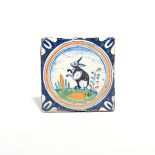 A Delft tile early 17th century, painted in shades of blue, green and ochre with a rabbit seated