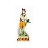 A Pratt ware figure of a young boy c.1800-10, standing with arms folded and leaning against a branch