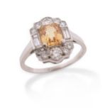 A yellow sapphire and diamond cluster ring, the emerald-cut sapphire set within a surround of