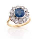 A sapphire and diamond cluster ring, the cushion-shaped sapphire is set within a surround of round