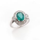 An emerald and diamond cluster ring, the oval shaped emerald flanked with round brilliant-cut