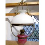 A 19th century lamp with cranberry font and milk white shade with brass frame
