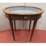 An Edwardian mahogany vitrine of oval form with plate glass top raised on four square taper supports