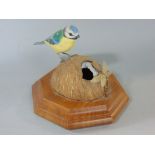 A life sized carved timber model of a blue tit astride a coconut accompanied by a dragonfly, set