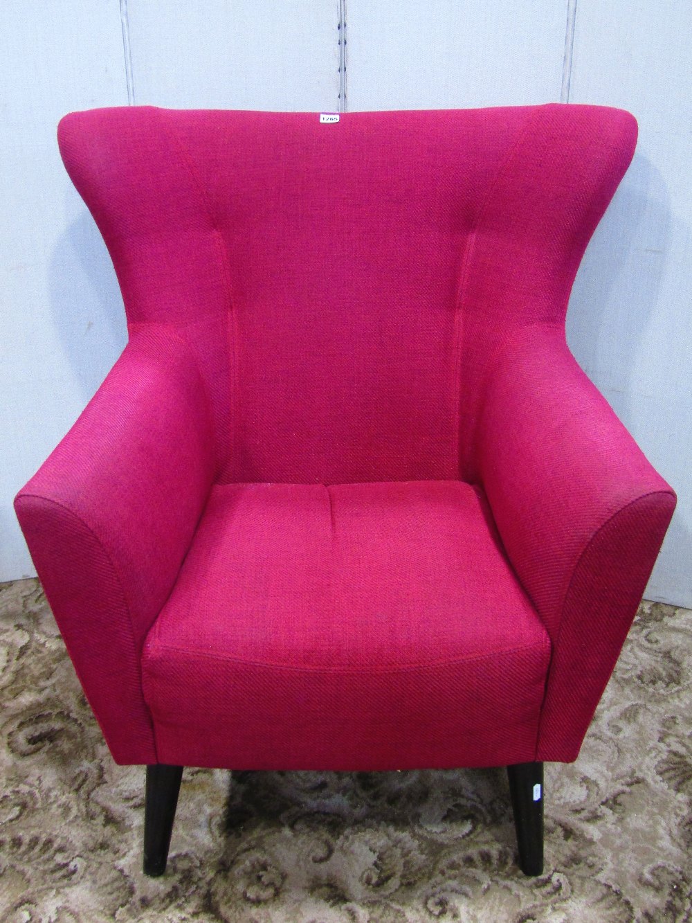 A retro/1950s style wing back armchair, with shaped outline and plum coloured upholstery, raised