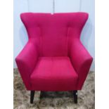 A retro/1950s style wing back armchair, with shaped outline and plum coloured upholstery, raised