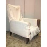 An Edwardian low deep seated armchair with simple rolled arms raised on square tapered forelegs with