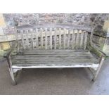 A weathered contemporary teak, three seat garden bench with slatted seat and back beneath a curved