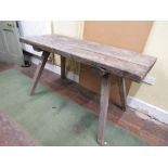 An antique rustic work table of rectangular form, the heavy plank top raised on four splay supports,