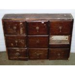 A vintage stained pine frame nest of nine drawers, presented in rows of three, 85cm wide x 20cm deep