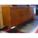 A long and low retro teak sideboard made by G W Evans Ltd, London, enclosed by three doors and tower