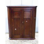 A Georgian oak hanging corner cupboard enclosed by a pair of rectangular panelled doors together