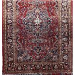 Persian rug with central blue medallion, framed by scrolled foliage upon a red ground, 180 x 125cm