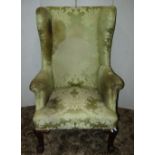 A Georgian style wing armchair with light green ground floral patterned upholstery, raised on claw