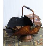 A 19th century copper helmet shaped coal scuttle with turned wooden hand grips together with