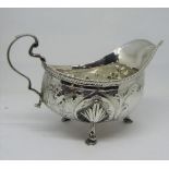A Georgian silver sauce boat with embossed repeating floral detail, scrolled handle, raised on three