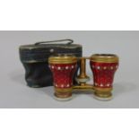 A cased pair of opera glasses in gilt brass and mother-of-pearl, the barrels with ruby red enamel