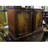 A pair of Victorian mahogany pedestal cupboards, each enclosed by a carved and moulded panelled door