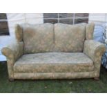 A traditional winged back three piece suite with rolled arms, floral patterned upholstery and