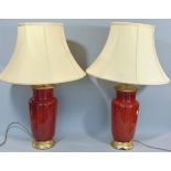 A pair of Chinese style ovi-form vases in ox-red glaze with gilded mounts, adapted as lamps,