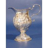 An embossed silver Georgian cream jug, the body of helmet form, raised on a waisted foot and
