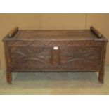 An oak box settle with rising lid, the panelled framework with repeating carved geometric detail,
