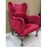 An Edwardian wing armchair in the Georgian manner, with upholstered finish, raised on carved