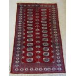 An Afghan red ground rug with multi-repeating white ground medallion panels within similar running