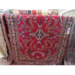 A red ground Persian style wool rug with abstract and floral detail within repeating borders 105 x