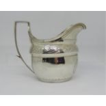 A Georgian silver cream jug of helmet shaped form, with repeating geometric band, within reeded