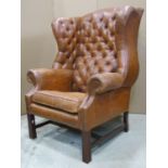 A Georgian style tan leather upholstered wing armchair, with button back, over a loose seat cushion,