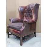 A Georgian style wing armchair with ox-blood coloured leather upholstery, buttoned back and